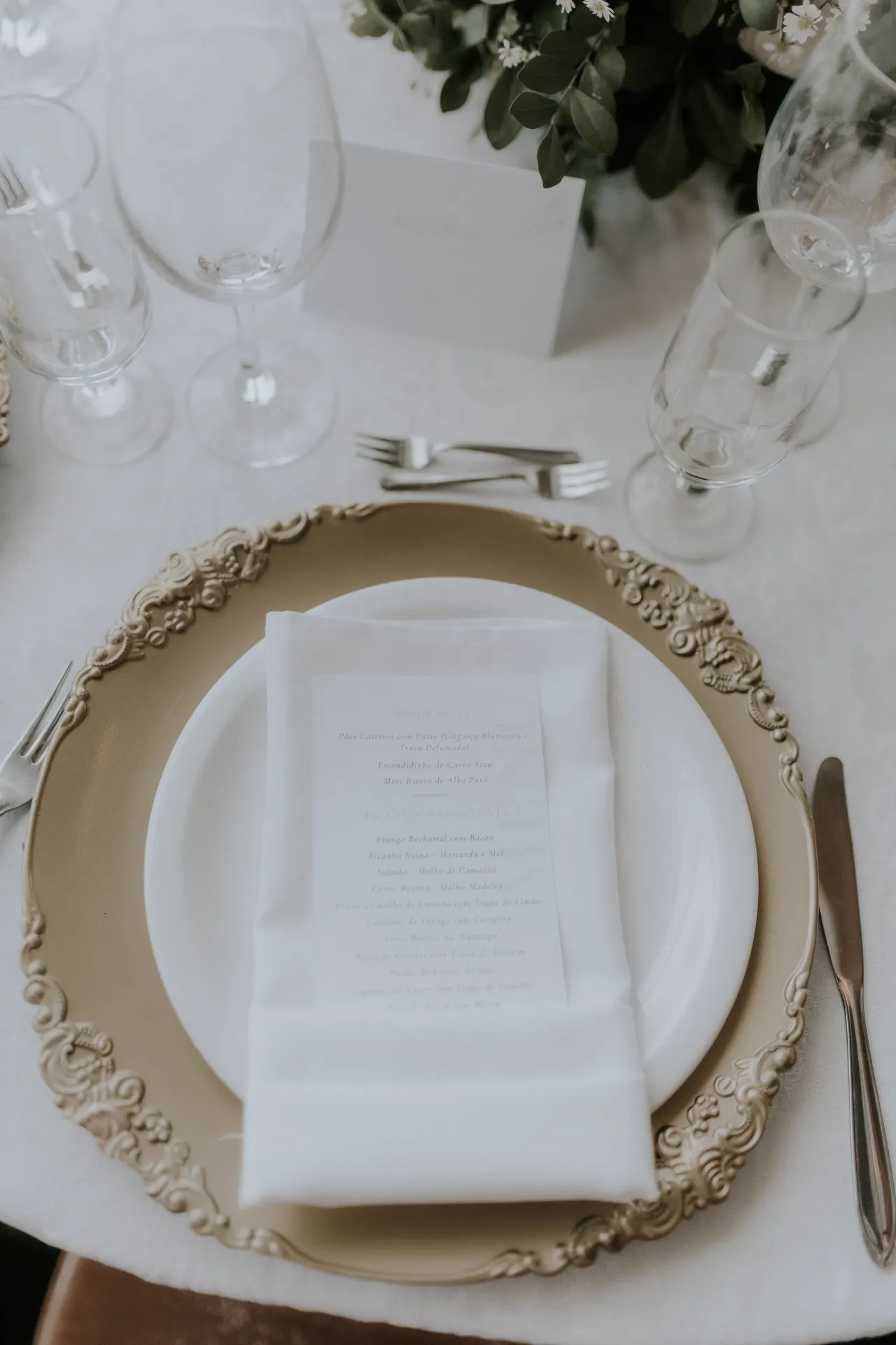 A place setting with a gold charger plate and a menu card.