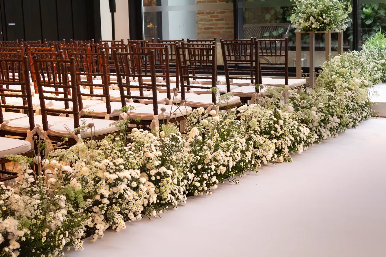 A ceremony aisle lined with white flowers and chairs.