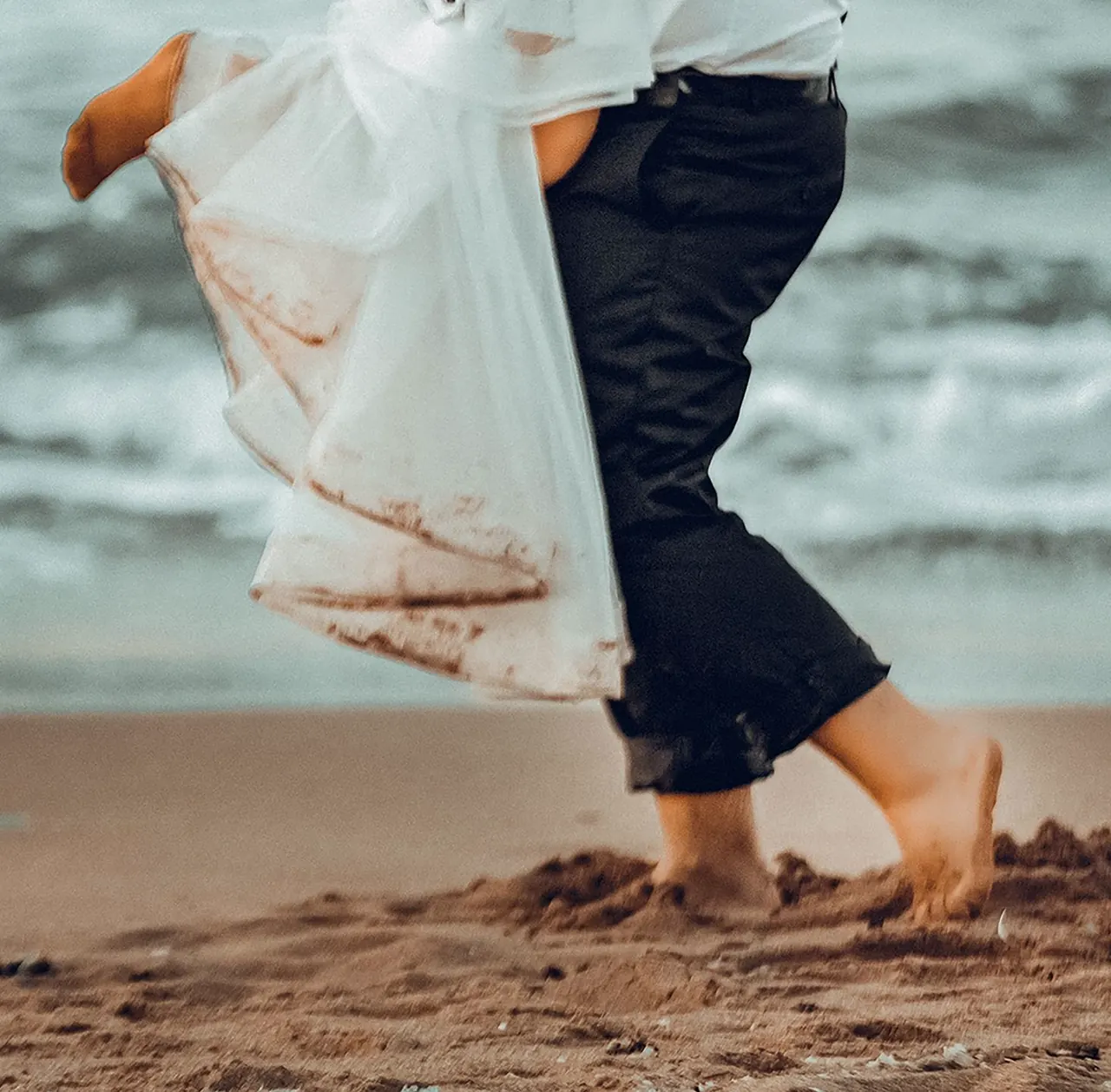 Bare feet in the sand and a wedding dress hem at the water's edge.